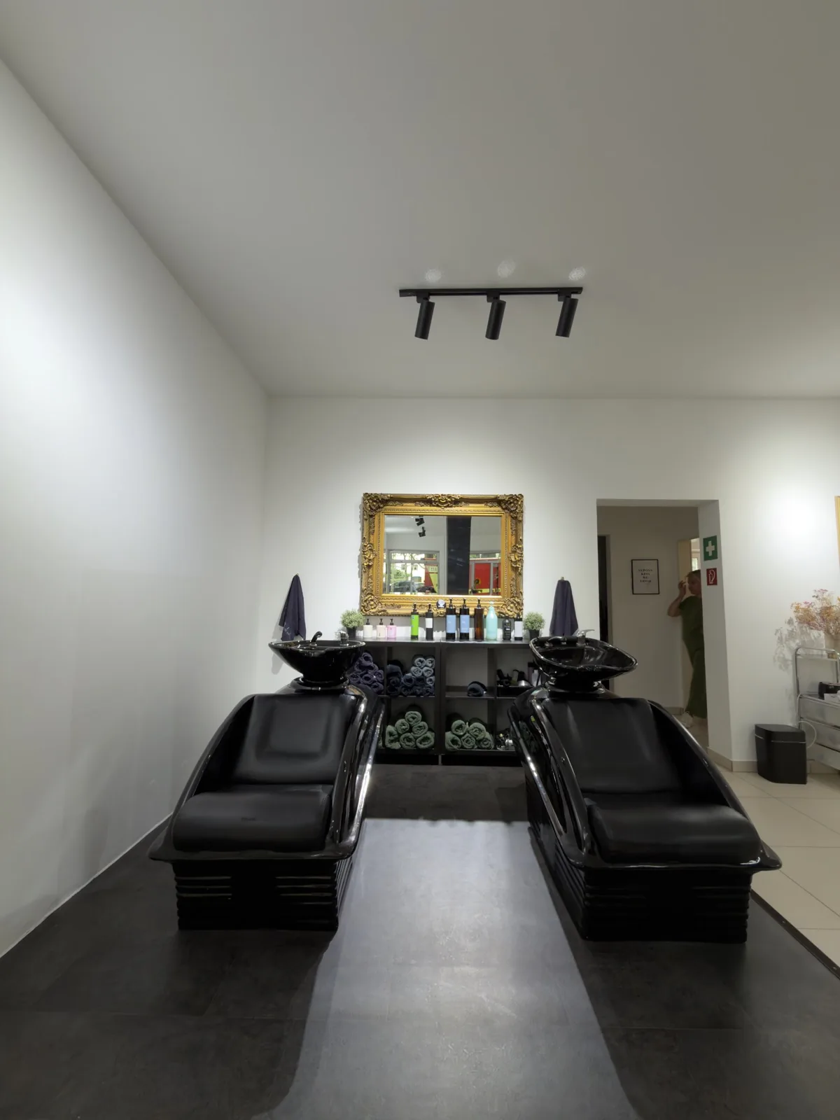 Waschbereich im Salon La Coiffeur mit schwarzen Waschliegen und goldgerahmtem Spiegel