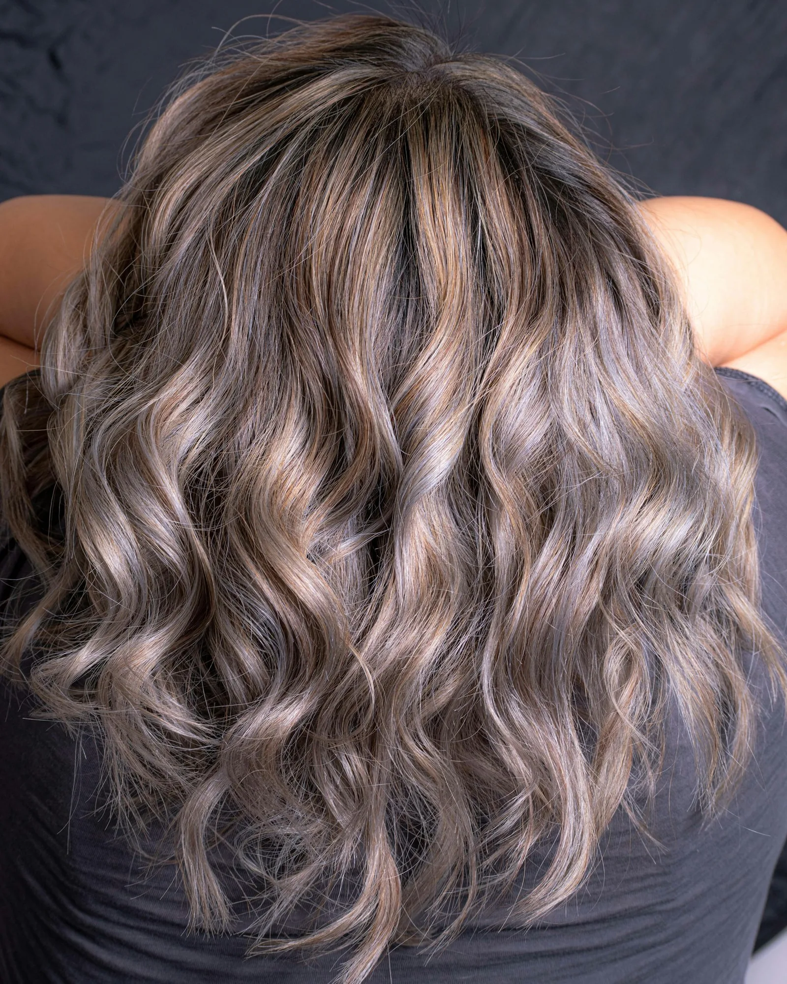 Aschblonde Wellen, edles Balayage-Ergebnis vor dunklem Hintergrund